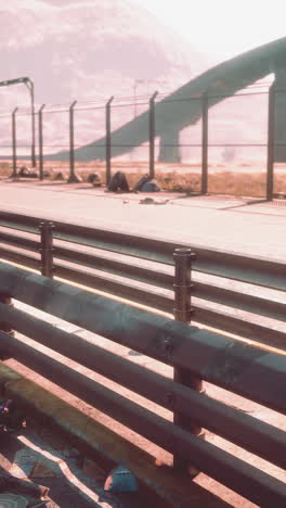 a rundown road with a futuristic metal bridge in the background