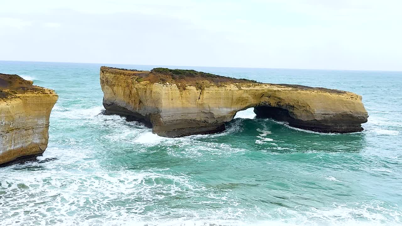 Dynamic ocean waves crash against rugged cliffs at Port Campbell, Australia. Captured in natural daylight with vibrant blues and greens