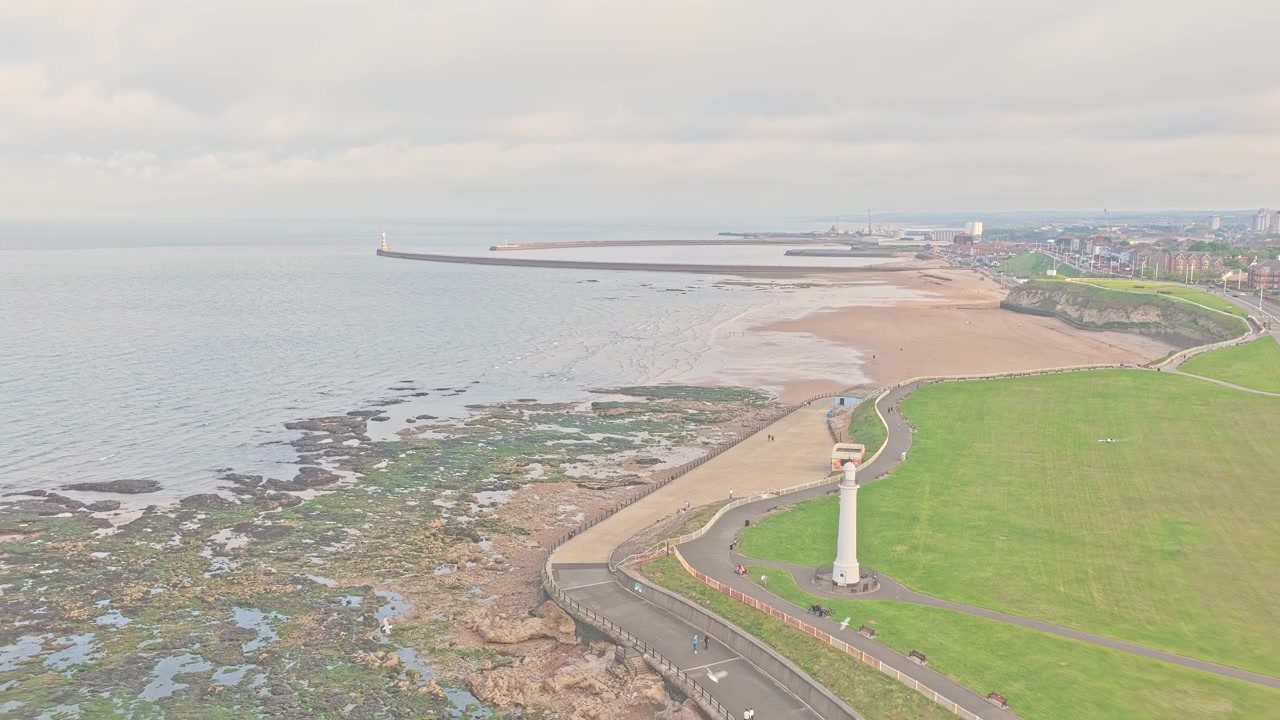Il faro di Roker si affaccia sul molo di Roker, Marine Walk e la spiaggia di Roker lungo il Mare del Nord a Sunderland, Tyne and Wear, rivelando l'ingresso del porto e la costa rocciosa, ripresa drone in allontanamento.
