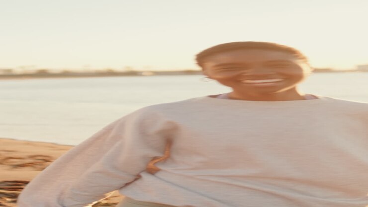Giovane donna felice che corre e sorride su una spiaggia al tramonto