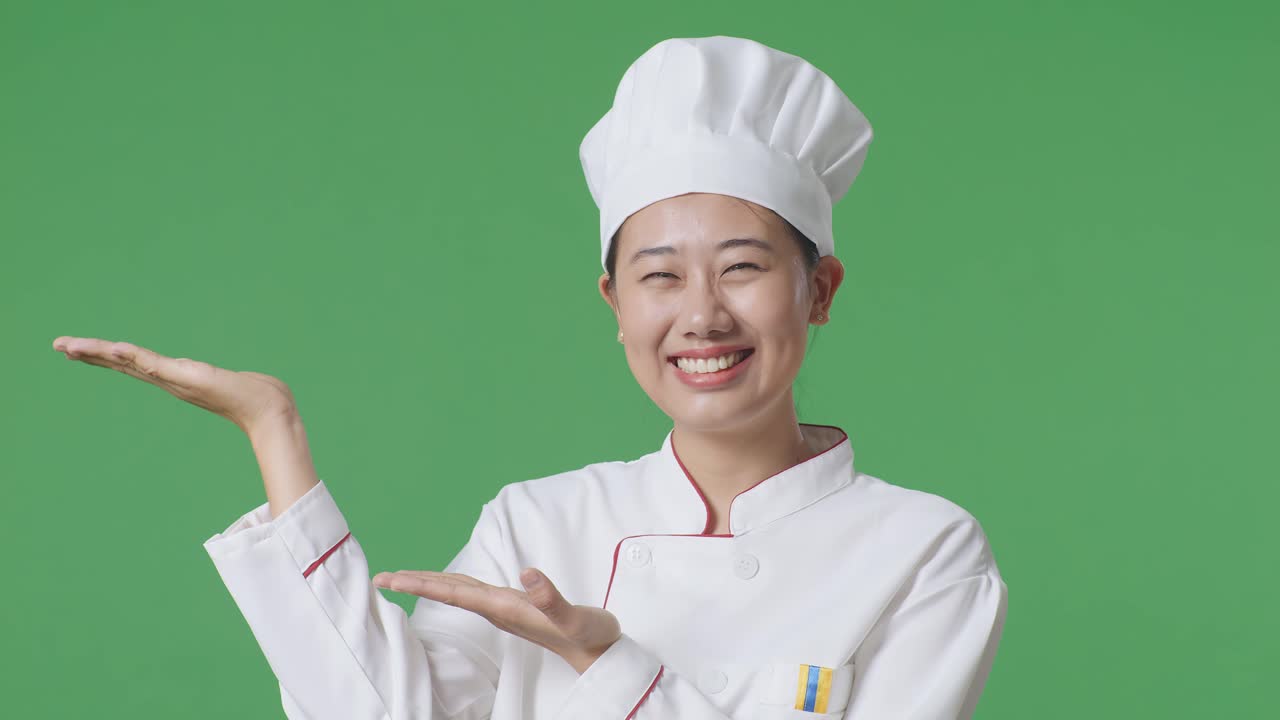녹색 스크린 배경 스튜디오에 서 있는 동안 웃고 을 가리키는 아시아 여성 셰프의 클로즈업