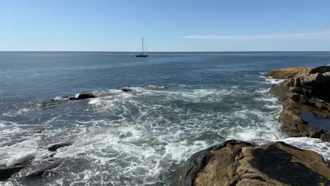 sailboat travels along rocky maine coastline