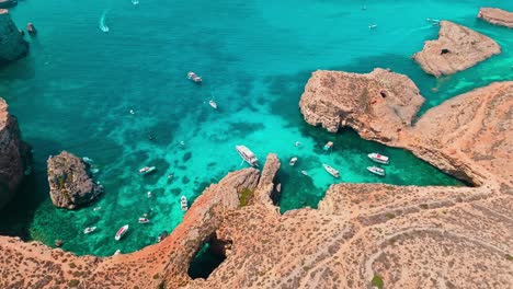 video aéreo de la laguna de cristal en malta, capturando barcos anclados en las impresionantes aguas turquesas rodeados de escarpados acantilados costeros