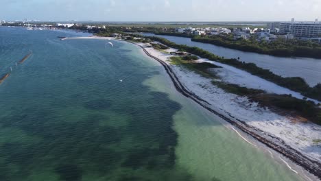 wide drone footage of the cancun coastline, aerial footage of hotels in the distance, and the oceanfront with clear blue ocean waters