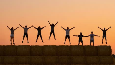 a joyful celebration of togetherness: friends jumping and cheering on hay bales against a beautiful sunset background in a perfect outdoor gathering