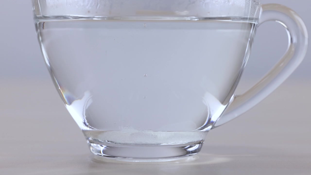 Toma macro de un terrón de azúcar blanco disolviéndose en agua clara con burbujas ascendentes