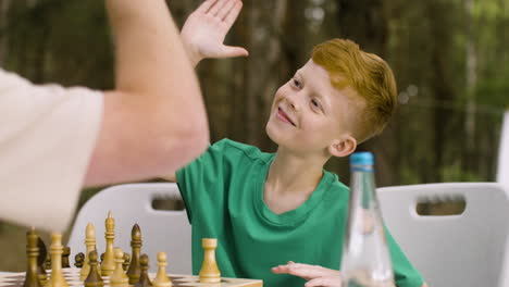 lindo niño jugando al ajedrez con su padre y dándole cinco en el campamento en el bosque