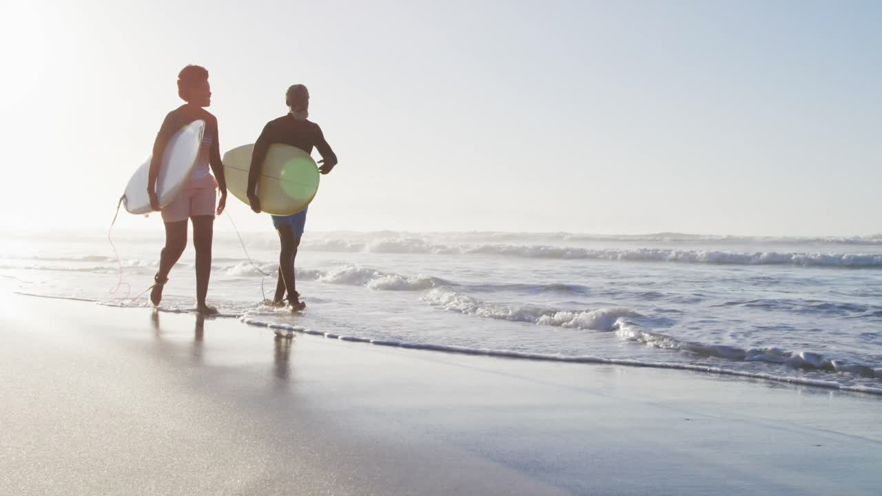 행복한 아프리카계 미국인 부부가  ⁇ 은 해변에서 서프보드와 함께  ⁇ 고 있습니다.