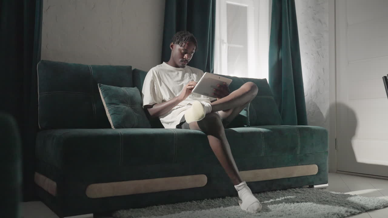 Champ relaxing on teal sofa, engrossed in tablet with natural light streaming through window. Peaceful, calm atmosphere in modern living room, perfect for focus and leisure time