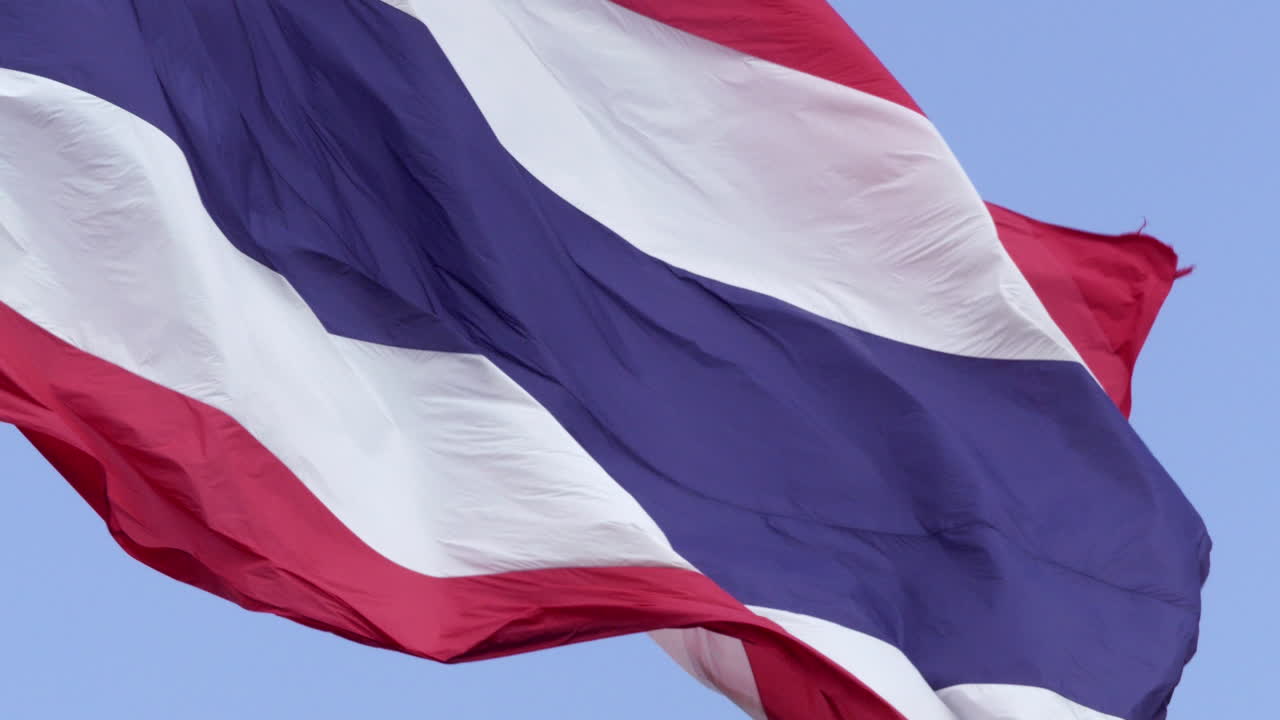 Slow motion capture of a large Thai flag swaying gently against the backdrop of a bright sky. The graceful motion of the Thai flag reflects the country’s strength, history, and cultural pride.