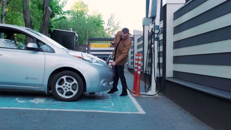 proceso de reabastecimiento de combustible de un automóvil eléctrico. un disparo debajo de la escotilla donde se carga el automóvil ecológico eléctrico. la escotella de carga del automóvil eléctrico se abre automáticamente. una mano masculina inserta un automóvil erecto