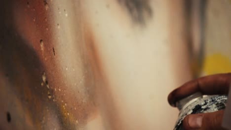 close up of a spray can artists hand as he carefully sprays a detailed mural in an art gallery