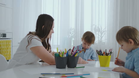 Mom-helps-sons-learn-to-draw-doing-homework-preschool-preparation-at-home-sitting-in-the-white-kitchen.