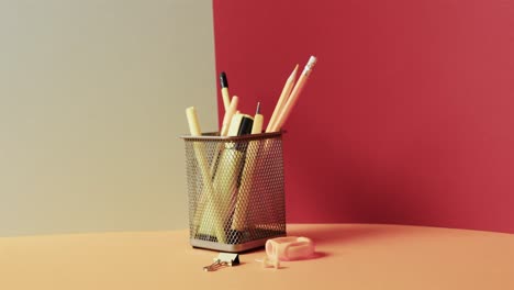Close-up-of-school-stationery-in-cup-with-copy-space-on-grey-and-red-background,-in-slow-motion