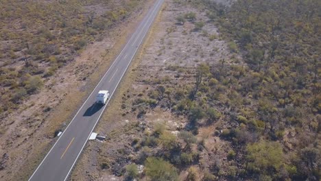 aerial track of a big white camper van driving through the desert in the mexico highway 1