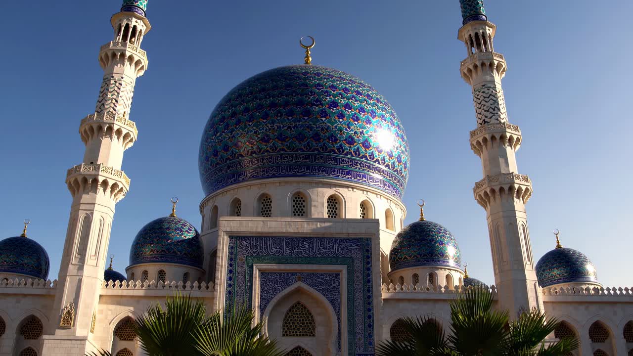 Un video riprende un'inquadratura dal basso di una grande moschea con cupole a mosaico blu finemente decorate e minareti.