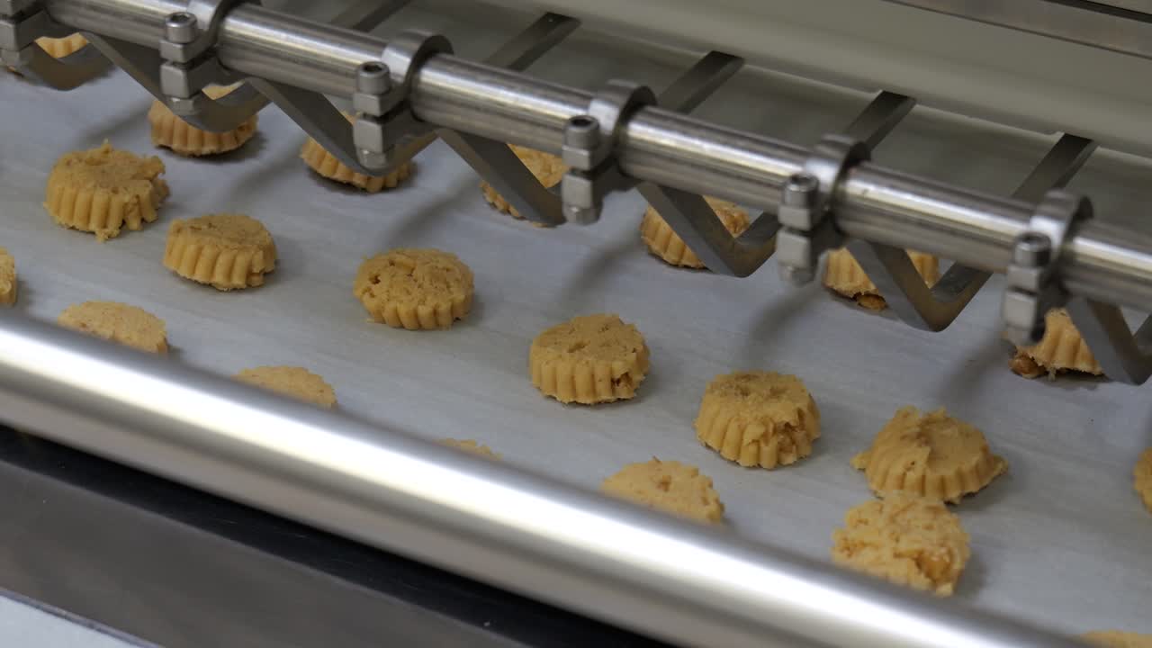 Close up of an industrial bakery machine placing raw biscuit dough pieces onto parchment paper on a metal tray in a French pastry production line