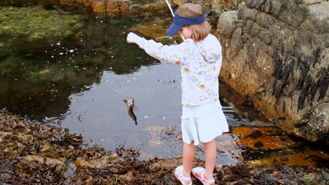 Junges-Mädchen-Hält-Stolz-Fisch-Hoch,-Den-Sie-Aus-Einem-Felsenpool-Im-Meer-Gefangen-Hat