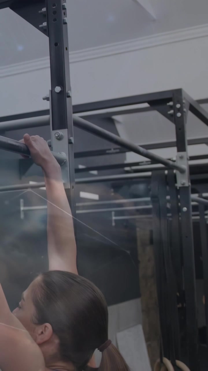 Vertical video: Hand entering left starting woman reaching pullup bar on rig pulling up for fitness