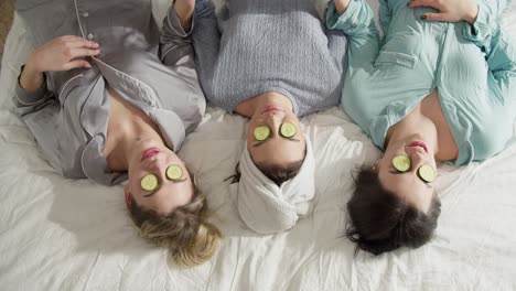 happy friends with cucumber mask relaxing on the bed with towels on head