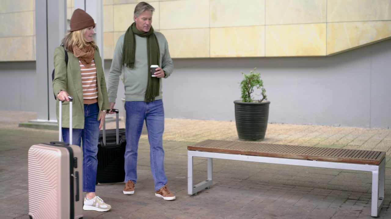 Een ouder echtpaar komt aan op een perron, trekt koffers, zit op een bankje, kijkt op de klok en wacht op vervoer.