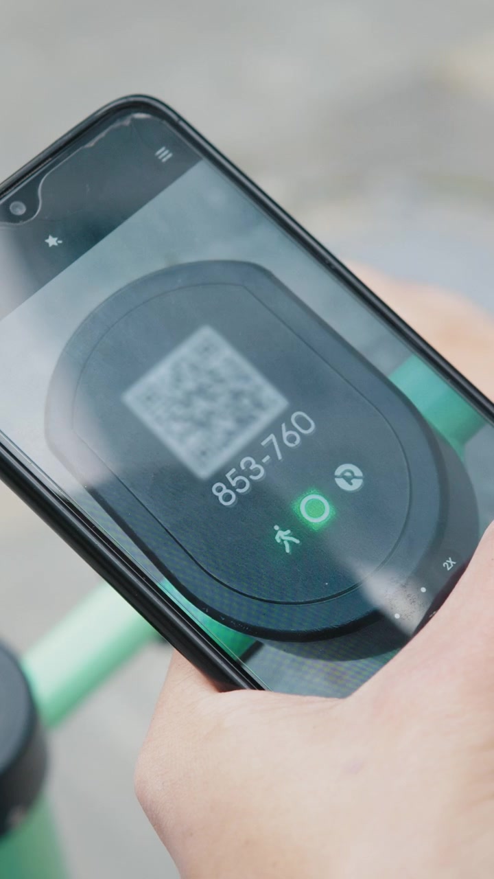 Una persona che usa uno smartphone per scansionare un codice QR; il telefono mostra un numero e una luce verde.