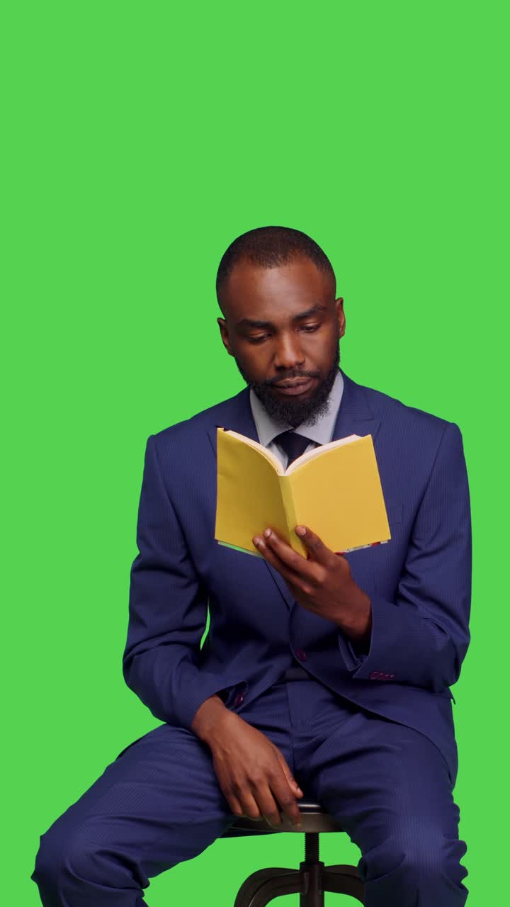 Vertical video: Front view of modern entrepreneur reading literature book in studio