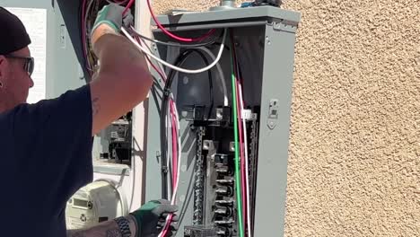 Technician-Running-Wires-Inside-Solar-Panel-Control-Box-On-Side-Of-House-for-solar-install