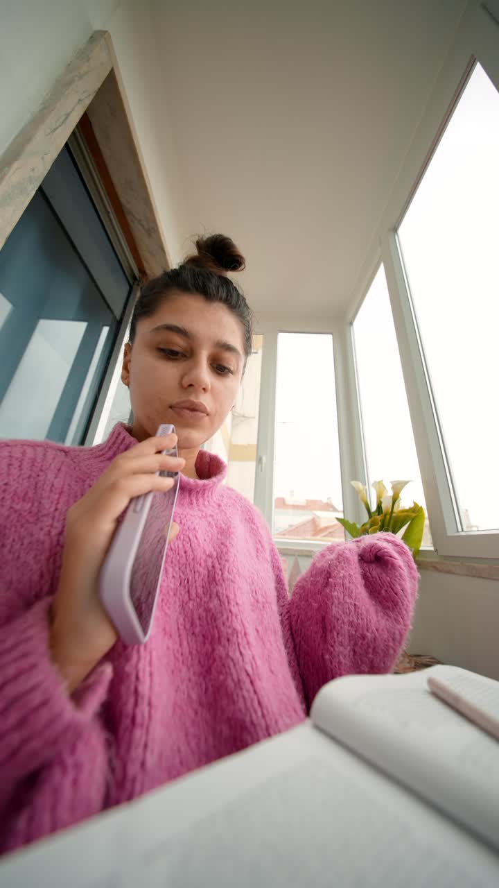Giovane donna che parla allo smartphone mentre studia a casa