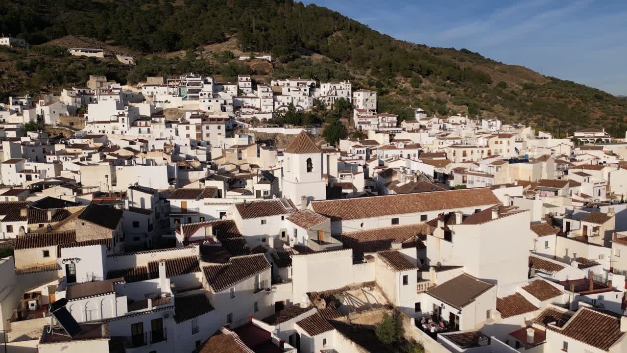 Pull out drone shot of an all white mountain village in Spain, Canillas de Aceituno. The city is quiet and serene. The shot starts with a small church in the middel of the frame.