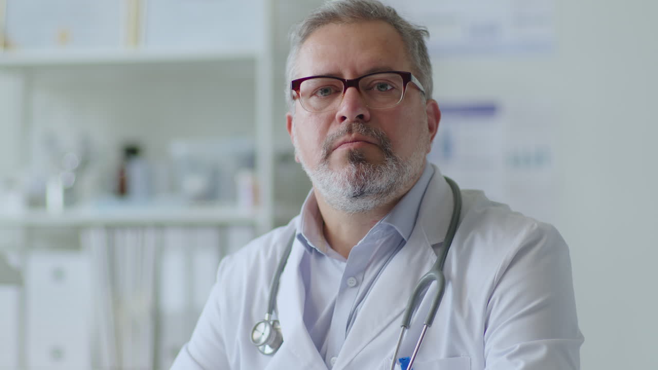 Portrait of Mid-Aged Male Physician Sitting at Workplace in Clinic