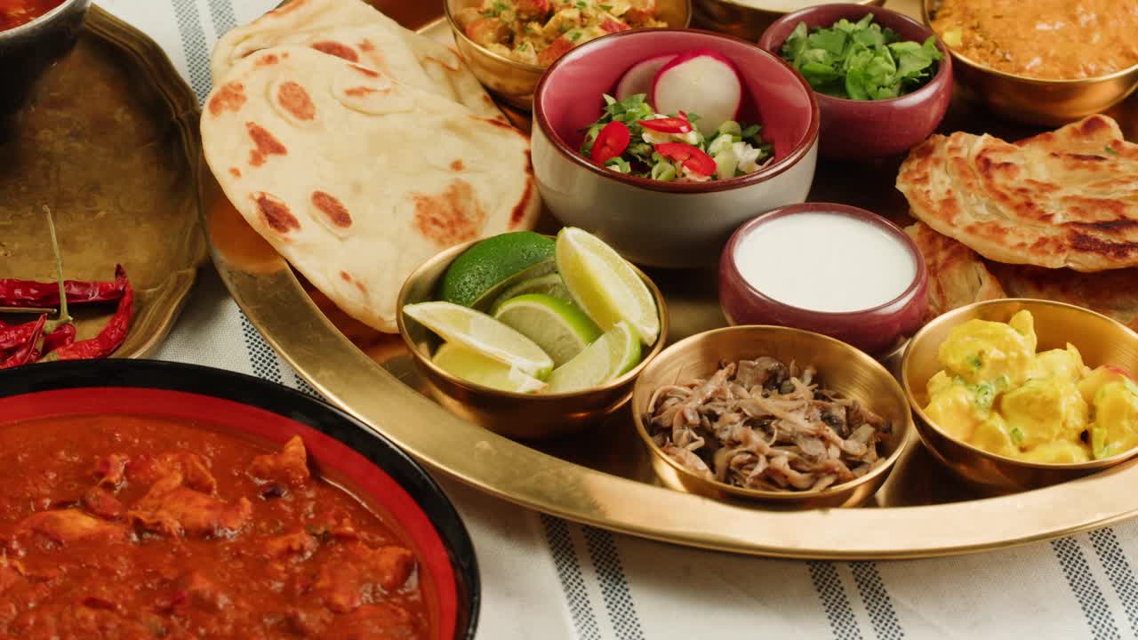 Assorted indian sri-lanka food set on wooden background. Dishes and appetisers of indeed cuisine, rice, lentils, paneer, samosa, spices, masala. Bowls and plates with indian food top view chicken. High quality 4k footage