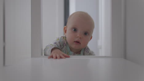 static view of a small caucasian girl clinging to a piece of furniture to get up