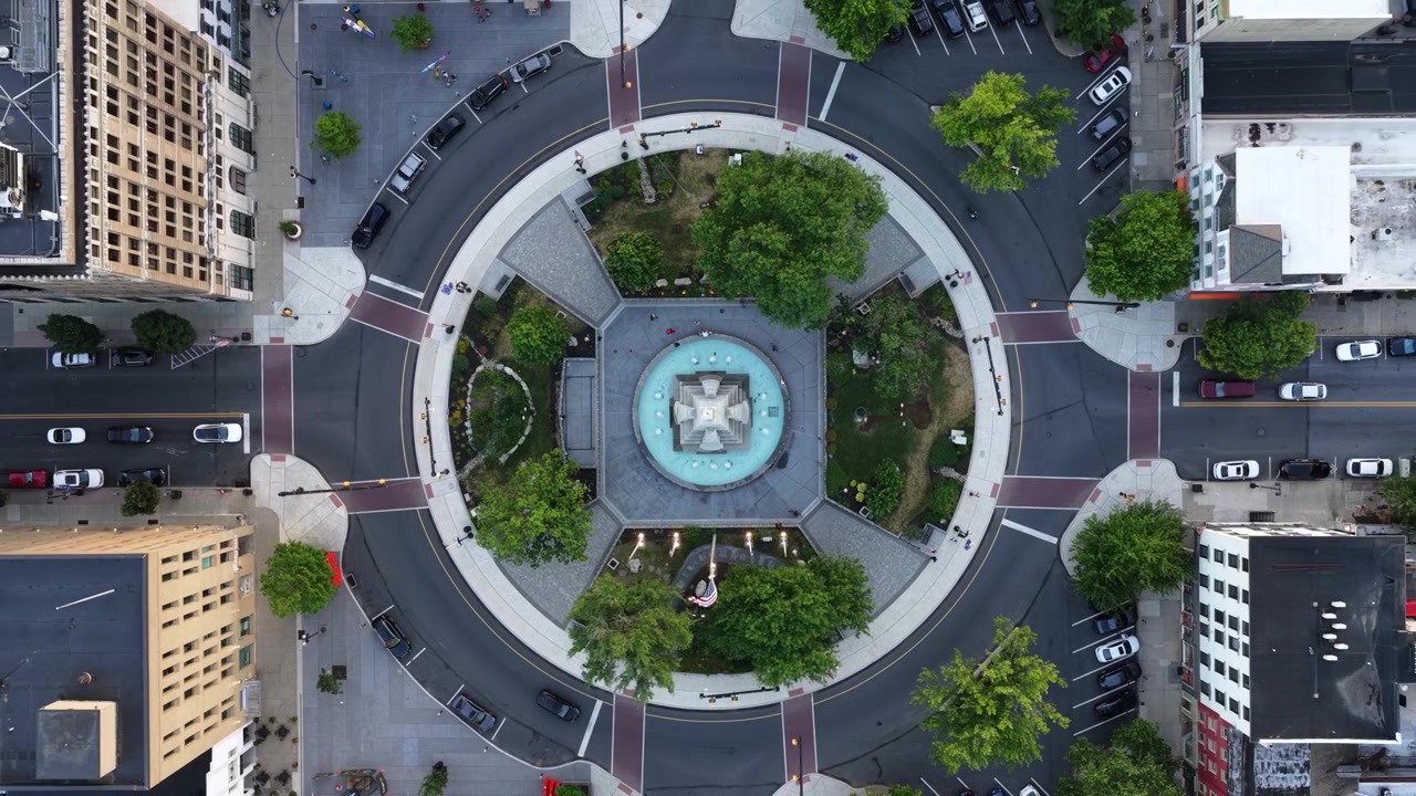 Fontana monumentale circolare in pietra al centro di una rotonda a Easton, Pennsylvania, alberi verdi simmetrici incorniciano una piazza pavimentata sotto alti edifici in mattoni circostanti. Ripresa aerea con drone in ascesa dall'alto