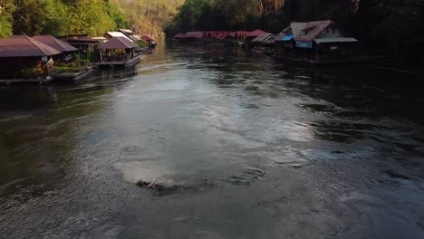 A-drone-shot-flying-fast-past-a-charming-floating-village-and-over-a-river-in-the-middle-of-the-jungle,-in-Sai-Yok-National-Park-in-the-province-of-Kanchanaburi-in-Thailand