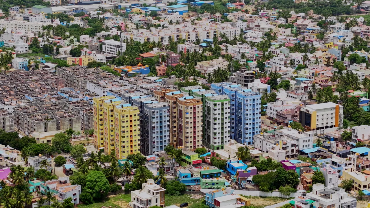 Vista aerea con drone di colorati appartamenti a molti piani circondati da densi edifici residenziali, case, alberi e strade attraverso una trafficata area urbana a Chennai, Tamil Nadu, India