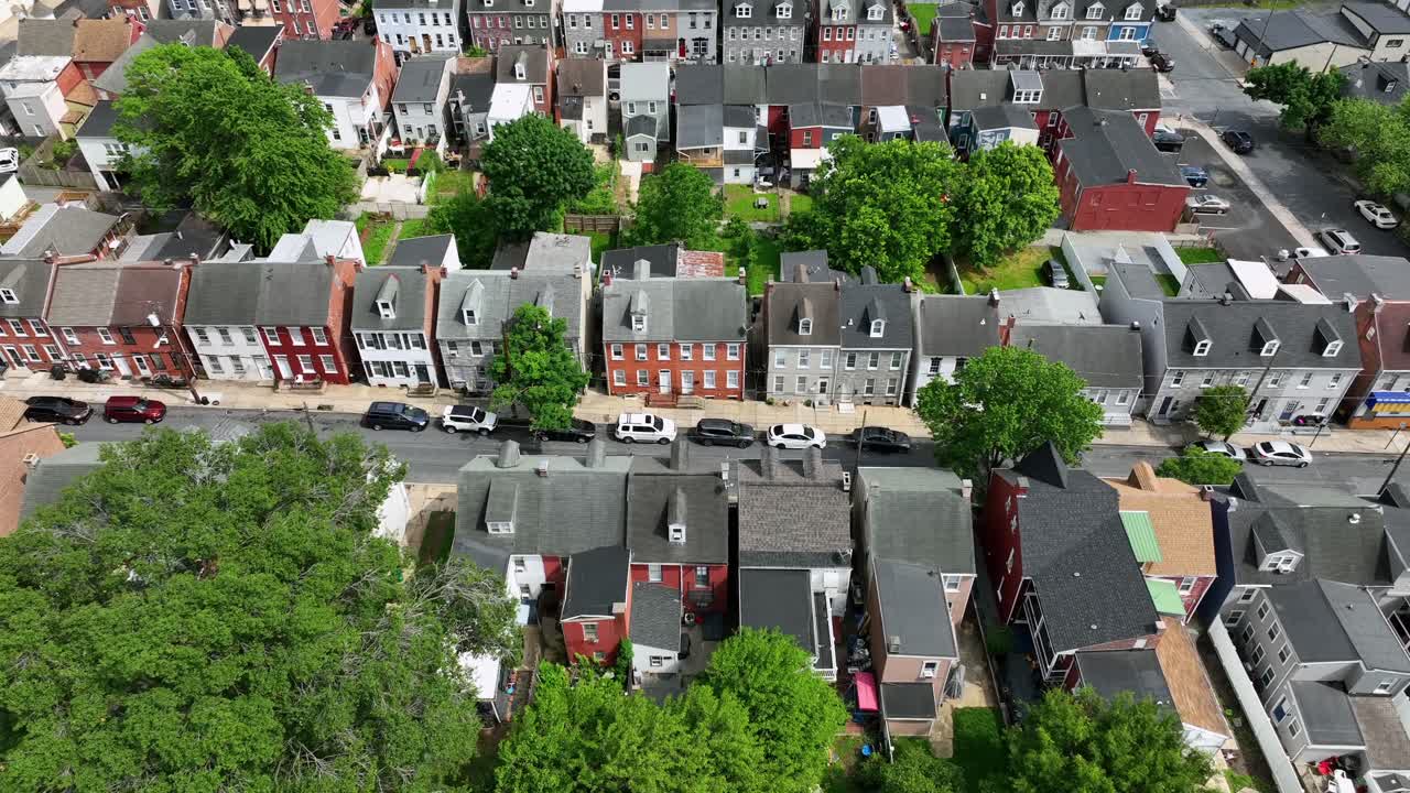 Aerial tilt down of american housing area with historic multi-family units and parking cars. Green trees and garden of american town. Sunlight in spring season.