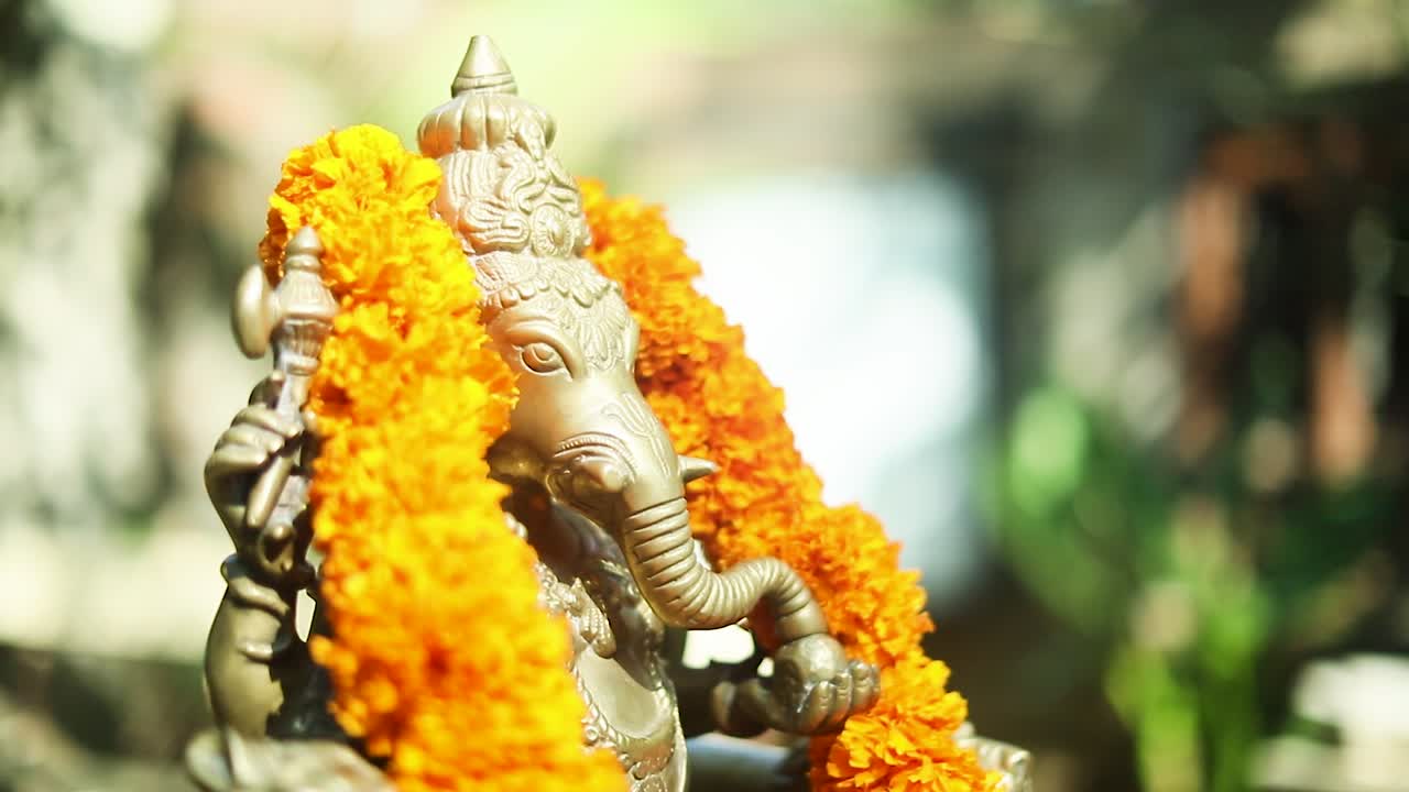 Closeup of Ganesha statue with a flower garland. Circle pan right, shallow focus