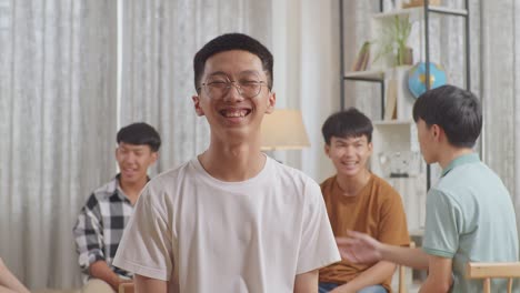 close up of a boy smiling to camera. asian teen group sitting in chairs forming a circle discussing at home