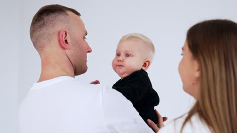 loving caucasian parents kiss their adorable baby on the cheeks. happy family portrait close up at white backdrop.
