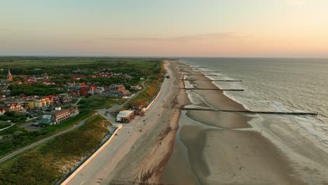 espectacular toma en órbita aérea de una playa interminable y un pequeño y pintoresco pueblo costero con tejados anaranjados durante la hora dorada