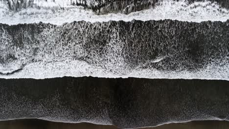 Aerial-static-drone-view,-waves-crash-or-break-on-black-sand-beach