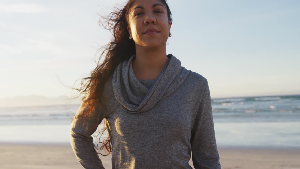 retrato de una mujer de raza mixta sosteniendo un tapete de yoga en la playa sonriendo