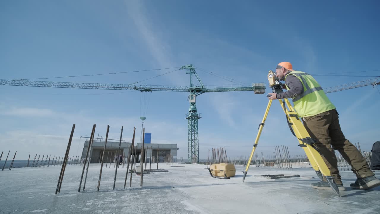 Geodetic works. Surveyor engineer in protective wear and red helmet using geodetic equipment at construction site. Professional equipment.