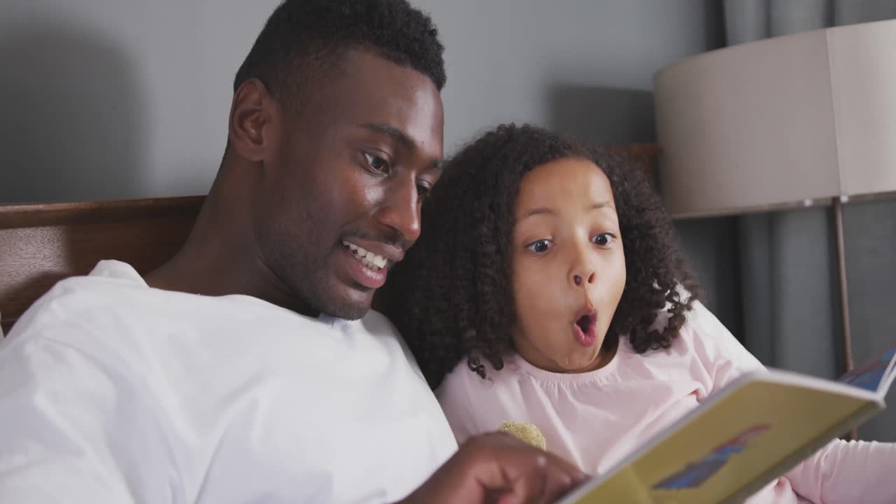 African american father reading a story to his daughter in bed