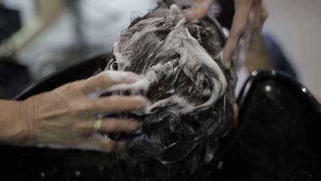 young girl lying on salon sink having her hair washed by professional hairdresser