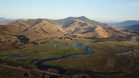 Aerial-of-river-in-Outback-Australia,-summer,-magic-hour,-blue-sky-reflected-in-large-river-at-foot-of-beautiful-mountains