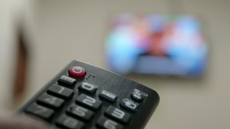 primer plano de la mano del hombre con el control remoto y viendo la televisión con prensas para cambiar el canal en el botón