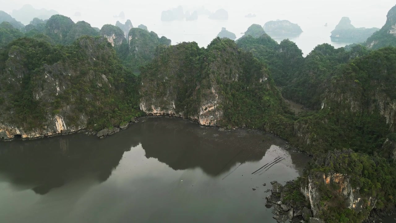 Cảnh quay bằng drone về những hòn đảo đá vôi karst tuyệt đẹp ở Vịnh Hạ Long với những vách đá lởm chởm, thảm thực vật tươi tốt và làn nước xanh ngọc bích tĩnh lặng được tăng cường bởi sương mù nhẹ, tạo nên một khung cảnh bờ biển điện ảnh ở Việt Nam