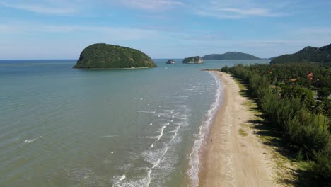 aerial footage towards the horizon revealing islands, blue sky, beachfront, waves rushing to shore